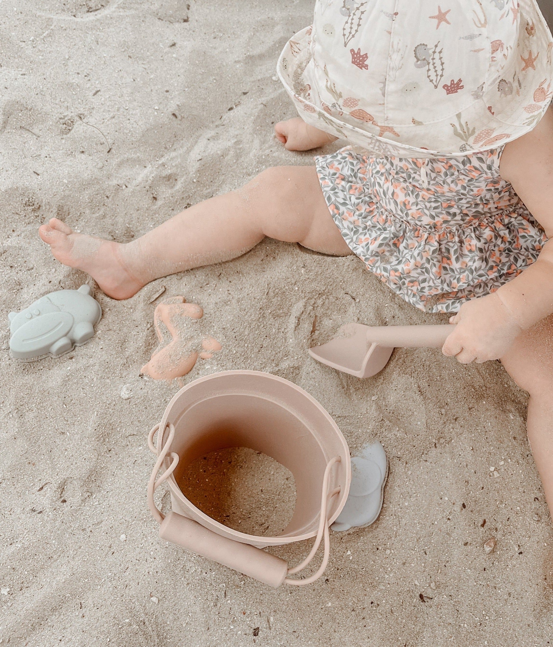 kind spelend op het strand met siliconen strandspeelgoed, strandemmer, zandvormpjes en zandschep.